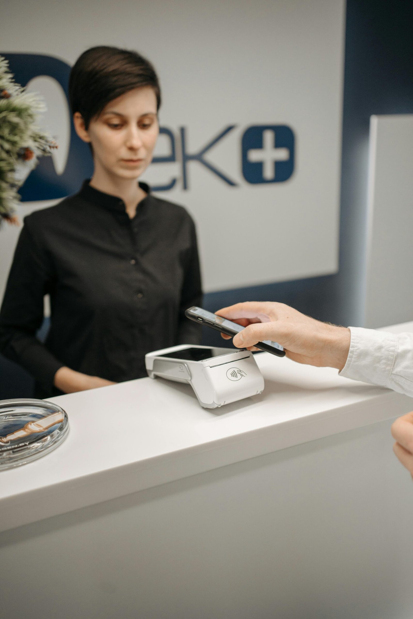 A woman witnesses a customer making a contactless payment using a smartphone at a service counter.